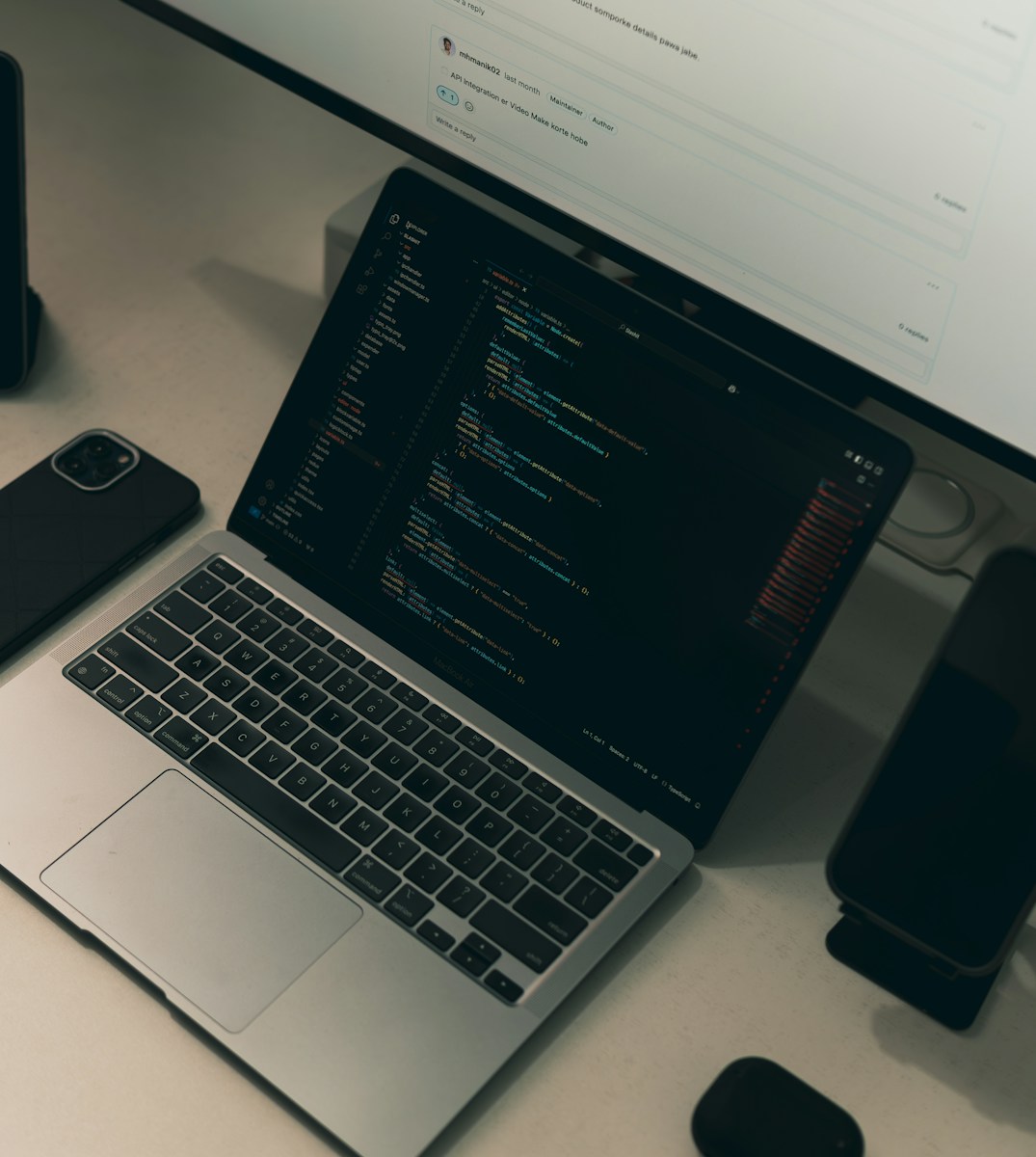 Laptop screen displays code with surrounding tech devices.